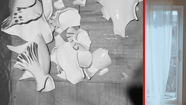 Shattered white ceramic pieces next to a sunlit window with sheer curtains.